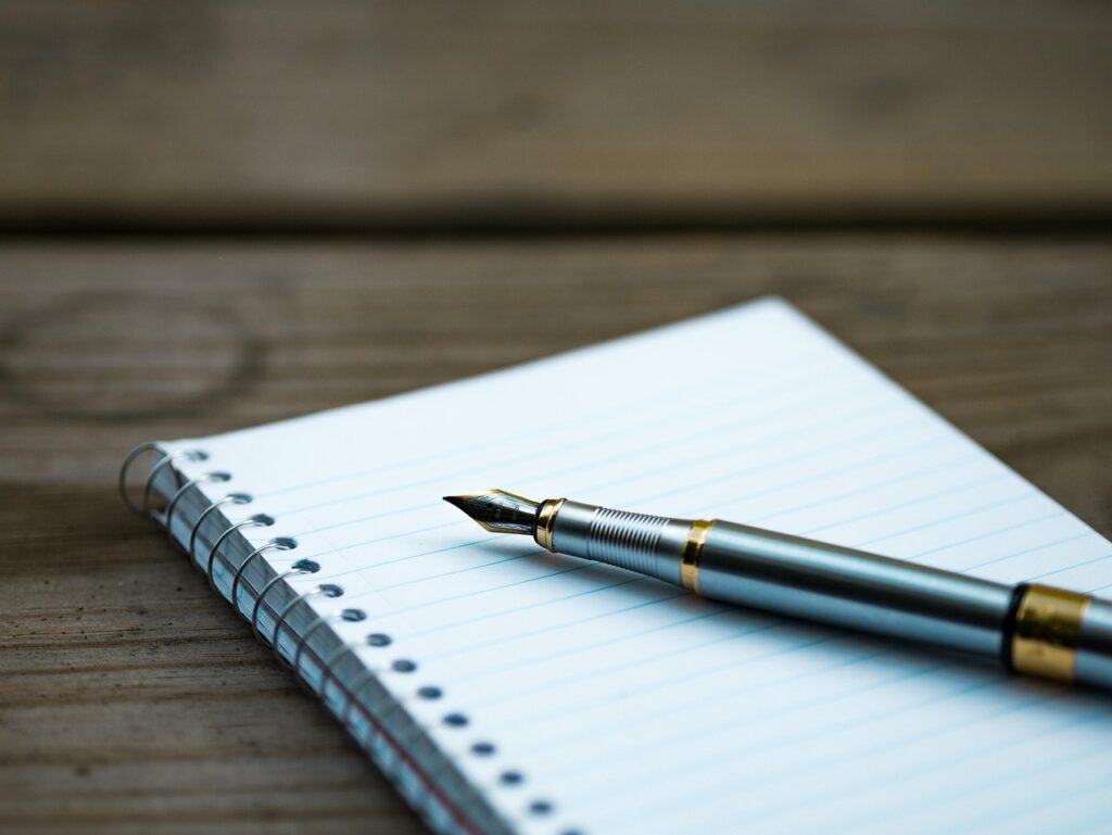 Fountain pen resting on a spiral notebook on a wooden table