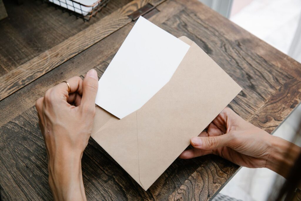 Hands holding a blank card and a kraft paper envelope on a wooden table