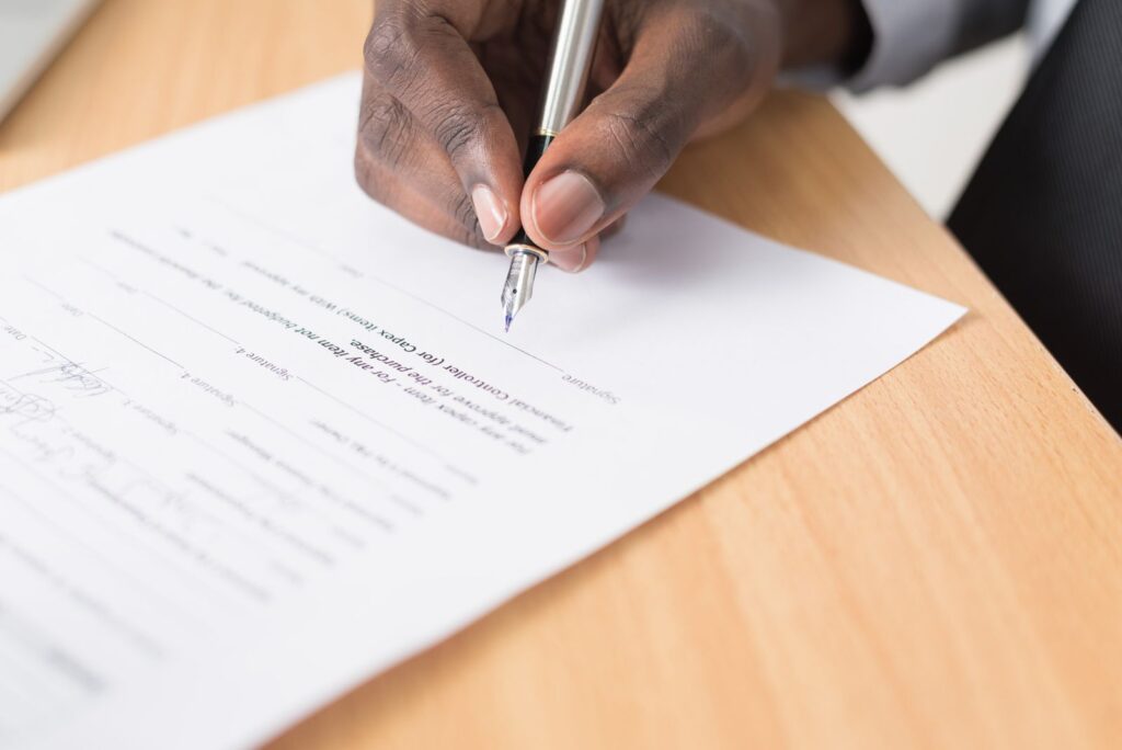 Hand signing a document with a fountain pen on a wooden desk